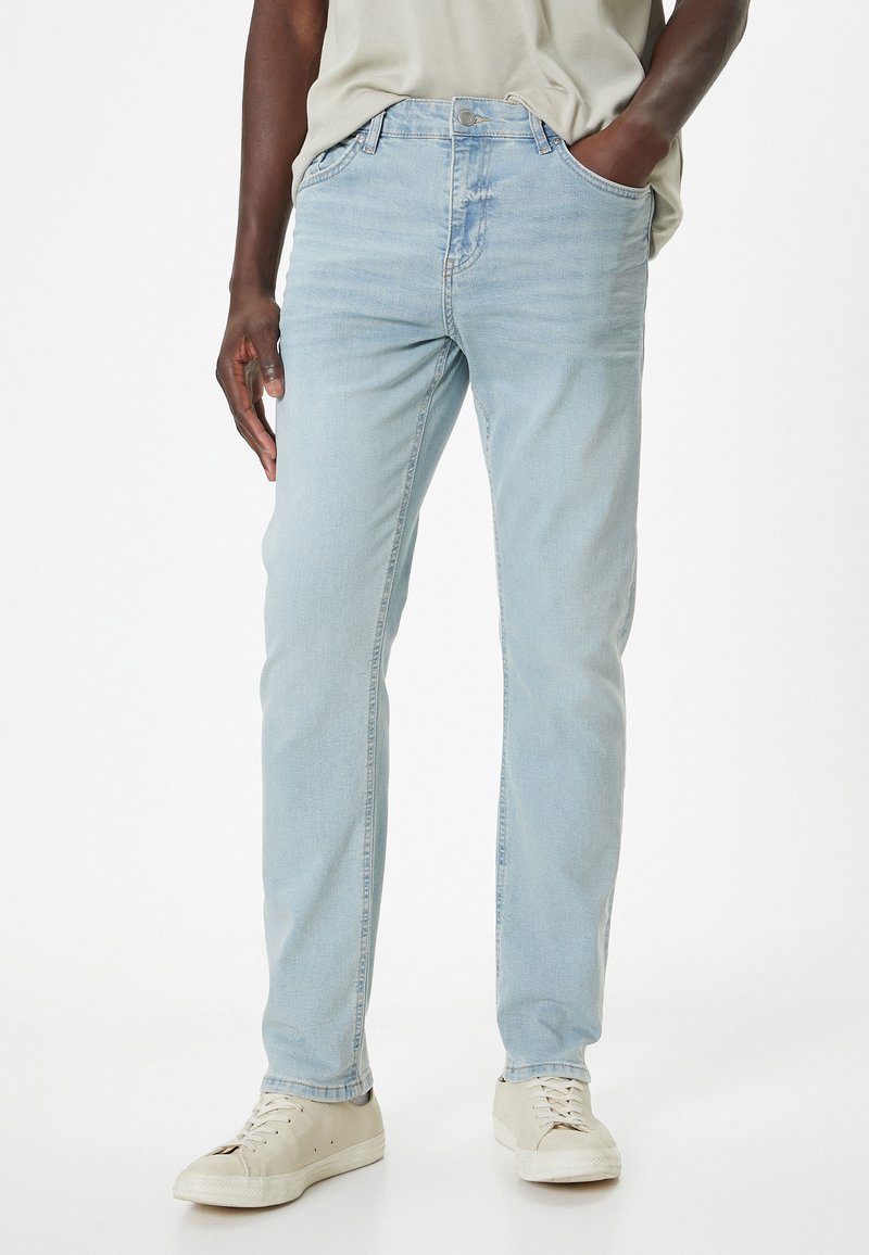 Jeans de mezclilla azul claro con diseño de pierna recta, cuatro bolsillos y una textura sutilmente desgastada. Llevados con zapatillas beige.
