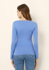 Camicia a maniche lunghe blu in tessuto morbido, con scollatura rotonda e design aderente, abbinata a jeans blu chiaro.