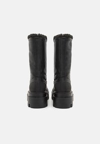 Botas altas negras con material de cuero suave, un suave collar de piel sintética y una suela gruesa y estructurada con estampado de marca.