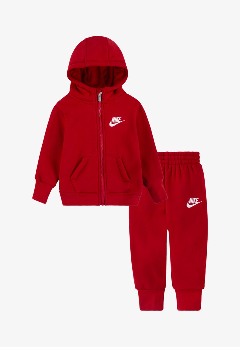 Piros Nike kapucnis cipzáras dzseki kenguruzsebbel és hozzáillő nadrág; mindkettőn fehér Nike logó található a mellkason és a combon.