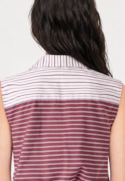 Femme vue de dos portant un débardeur à rayures horizontales blanches et bordeaux et des cheveux ondulés brun foncé.