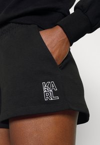 Černé bavlněné kraťasy s malým bílým vyšívaným logem "KARL" na kapse. Design zahrnuje hladkou texturu a volný střih.