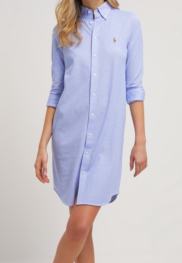 Helles blaues Hemdkleid mit langen Ärmeln, die an den Bündchen aufgerollt sind, mit einem kleinen Logo auf der Brust und einem geraden Saum.
