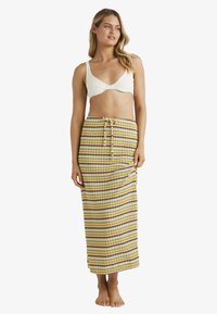 Gestreepte maxirok in geel, groen en wit met knopen en een koord in de taille; gedragen met een witte crop top.