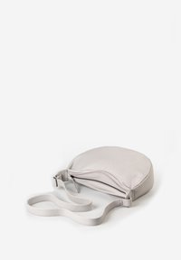 Light grey leather crossbody bag with a rounded design, zip closure, and flat adjustable strap. Smooth texture and minimalistic style.
