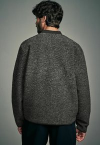 Donkergrijze fleece sweatshirt met een ronde halslijn, geribbelde details bij de kraag en een relaxte pasvorm. Zichtbare textuur en stiksels.