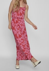 Red maxi dress with pink floral pattern, spaghetti straps, elastic waist, and a flowy silhouette. Worn with cream platform shoes.