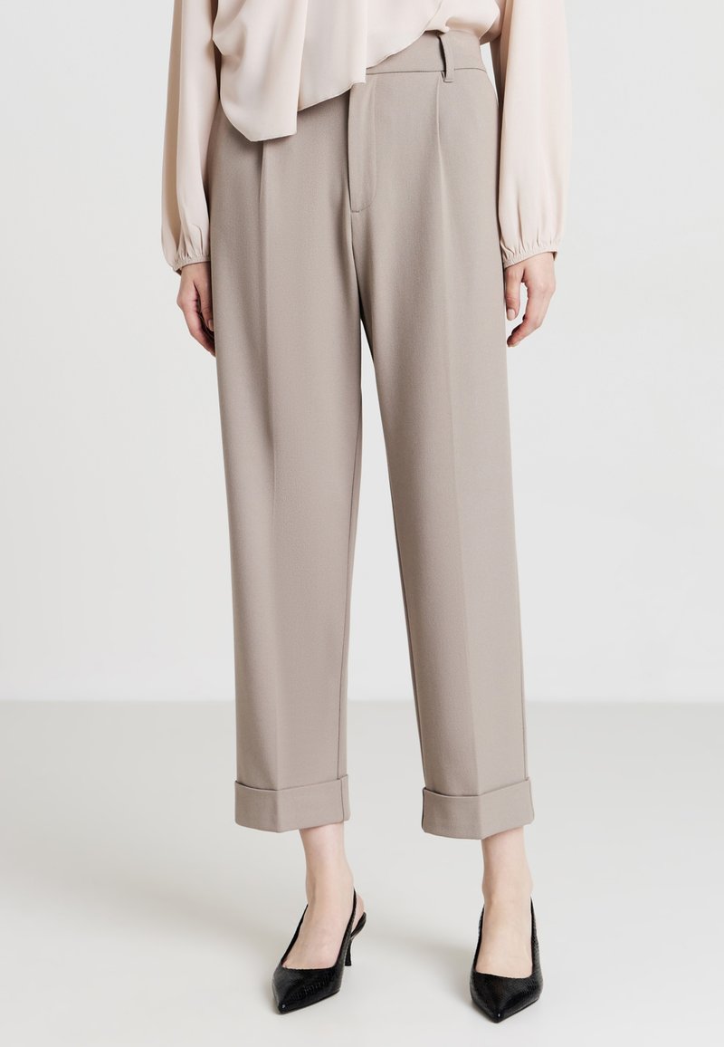 Pantaloni beige su misura con una vestibilità rilassata, dotati di orli cuffi e una superficie liscia, abbinati a décolleté nere a punta.