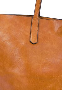 Tote bag van tan leer met een gladde textuur, voorzien van een enkele bovenhandgreep en contrasterende zwarte stiksels langs de randen.