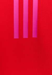 Fondo rojo texturizado con tres franjas verticales rosas. La superficie presenta un sutil patrón de cuadrícula para mayor detalle.