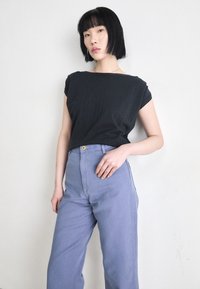 Top preto de mangas curtas com um decote largo, combinado com calças de cintura alta em azul claro, apresentando um detalhe de botão dourado à frente.