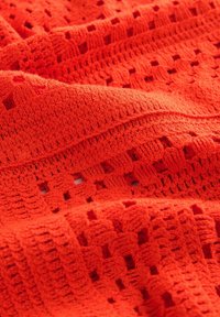 Oranžová háčkovaná látka s mnoha vzory, zobrazující otevřené stehy a texturované žebrování. Měkká, lehká a živá barva.