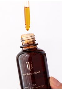 Bottiglia di vetro ambrato contenente olio con contagocce; il testo sull'etichetta include "TRUE BOTANICALS," "clear," e "PURE RADIANCE OIL."