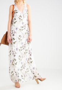 Robe longue en tissu léger avec un motif floral vert et violet. Dotée d'un décolleté en V profond, sans manches, avec des accents en dentelle.