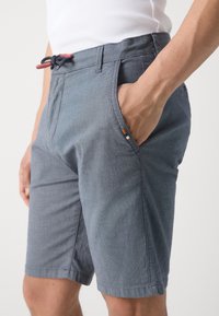 Shorts gris en tissu texturé, dotés d'une ceinture à cordon avec une extrémité rouge, de poches latérales et d'un petit détail de marque.