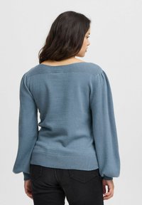 Pull en tricot bleu avec des manches longues bouffantes et un col large côtelé. Ourlet côtelé, texture lisse, conçu pour une silhouette ajustée.