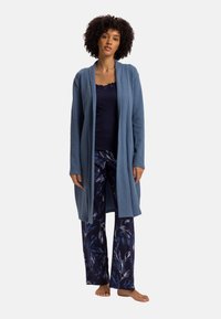 Cardigan lungo azzurro chiaro su una canotta navy, abbinato a pantaloni scuri con pattern che presentano disegni di foglie bianche; texture di tessuto morbido.