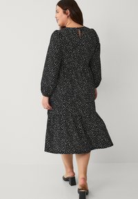 Czarna sukienka z długimi rękawami, zdobiona rozproszonym białym nadrukiem, z zaznaczoną talią, warstwowym dołem i małym otworem w kształcie klucza z tyłu.
