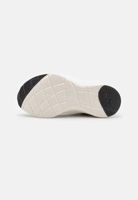 Shoe outsole featuring a textured white base with a black rubber heel. Designed with various tread patterns for grip and support.
