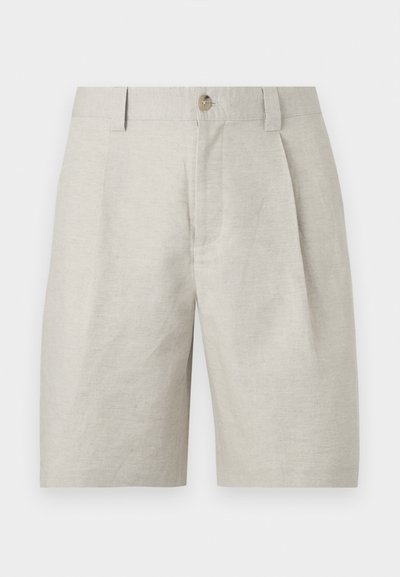 Short beige sur mesure avec plis à l'avant, passants pour ceinture et fermeture à un seul bouton à la taille.