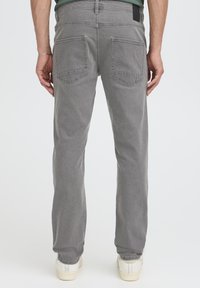 Szürke farmernadrág egyenes szabással, két hátsó zsebbel és fekete címkével a derékrészen. Texturált anyag minimális díszítéssel.