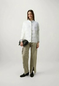 Weiße Pufferjacke mit horizontaler Steppstruktur, leichtgewichtig, kombiniert mit hellbeigen Cargo-Hosen mit Reißverschlussakzenten und einer schwarzen Handtasche.