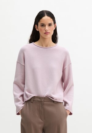 Pull en tricot rose clair avec un col rond et des manches longues, associé à un pantalon tailleur marron, mettant en valeur une coupe décontractée et une texture subtile.