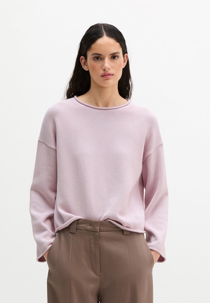 Light pink knit sweater with a round neckline and long sleeves, paired with brown tailored trousers, showcasing a relaxed fit and subtle texture.