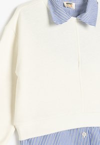 Felpa crema con orlo a costine combinata con un colletto a righe blu e bianche, con un taglio semplice e una texture.