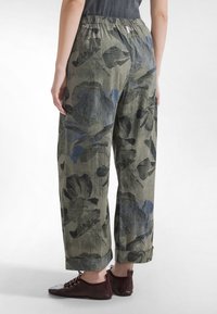 Luźne, oliwkowozielone spodnie zdobi kwiatowy wzór w odcieniach niebieskiego i czarnego. Model ma elastyczną talię oraz szerokie nogawki.