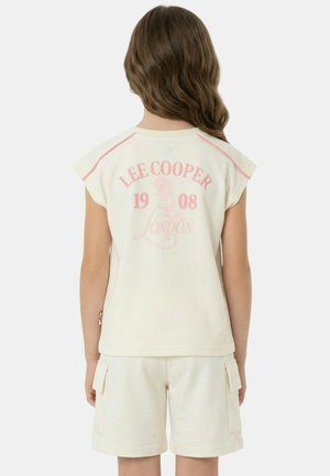 Enfant aux cheveux bruns ondulés portant un haut sans manches crème avec le texte rose "Lee Cooper 1908 London" et un short cargo assorti, vu de dos.