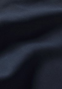 Tessuto di un blu navy con una superficie liscia, caratterizzato da una leggera lucentezza e da un motivo di trama diagonale, che si drappeggia dolcemente in pieghe naturali.