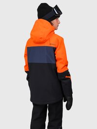 Persona con berretto nero e occhiali che indossa una giacca da sci a blocchi di colore arancione, blu navy e nera, con guanti neri, rivolto di lato.