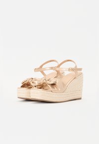 Beige wedge sandaalit, joissa on satiininen nauha, kultaa kudottu jutee alusta ja nilkkaremmi solkikiinnityksellä.