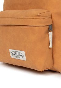 Cognackleurige leren rugzak met een voorvak, zichtbare stikseldetails en een wit label met het Eastpak-logo. Gevoerd oppervlak.