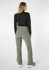 Khaki broek met een hoge taille, gladde textuur en zijritsen, gecombineerd met een zwart shirt met lange mouwen dat van achteren wordt gedragen.