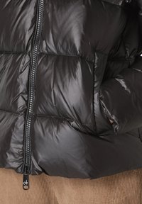Svart vadderad jacka med en glänsande yta, horisontella quiltade sektioner och en framficka med dragkedja och dragflik.
