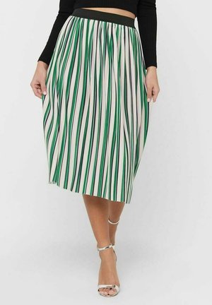 Femme portant une jupe midi plissée avec des rayures verticales vertes, bleues et blanches, associée à des talons à bride argentés et un top noir.
