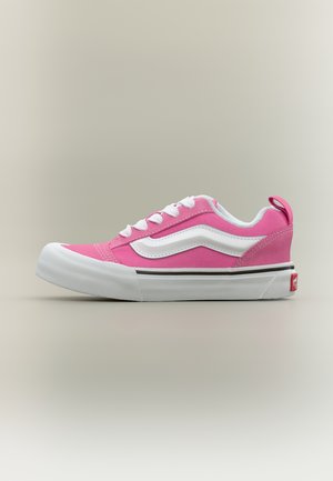 Baskets basses roses avec lacets blancs, une bande blanche sur le côté, une semelle épaisse blanche, et une étiquette logo rouge sur un fond neutre.