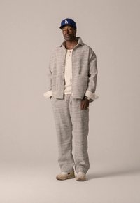 Pelēkas teksturētas adītas jaciņas un atbilstošas bikses ar viegla adījuma krēmkrāsas topu, savienotas ar zilu cepuri un bēšām sporta kurpēm.