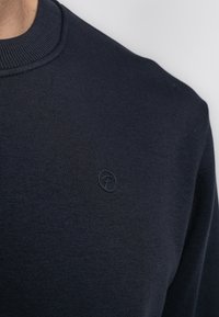 Navyblauw katoenen sweatshirt met een geribde ronde hals en een klein, reliëflogo op de borst. Zachte textuur met een eenvoudige uitstraling.