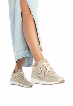 Zapatillas beige de cuero perforado, con detalles dorados y un tacón en cuña. Parte superior texturizada y cordones planos. Falda de mezclilla con dobladillo deshilachado visible.