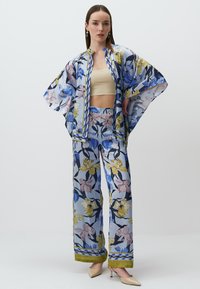 Kimono w kwiatowy nadruk w niebieskie, żółte i różowe kwiaty, zestawiony z pasującymi spodniami o szerokich nogawkach. Przezroczysty materiał z ozdobnymi brzegami.