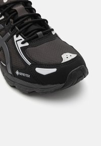 Schwarze und graue Sportschuhe aus Gore-Tex-Material, mit strukturiertem Mesh-Obermaterial, kontrastierenden weißen Akzenten und einer robusten Außensohle für guten Halt.