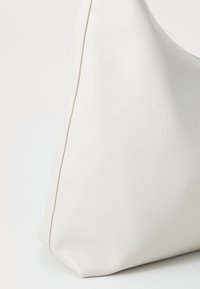 Gros plan sur un sac à main en cuir blanc lisse montrant le coin inférieur et la couture latérale sur un fond blanc.