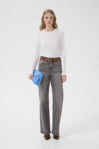 Ung kvinne iført hvit langermet skjorte, høytlivs grå jeans, brunt belte, brune spisse sko, holder en blå clutch-veske.