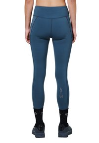 Blauwe hoge taille legging met een gladde textuur, zijnaad en "ATW" logo. Vermengd met zwarte sokken en sport schoenen.
