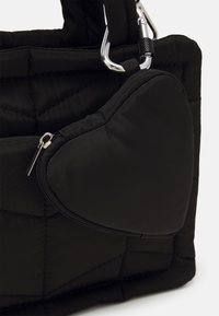 Sac en tissu matelassé noir avec une pochette zippée en forme de cœur attachée par un mousqueton argenté.