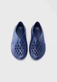 Navyblauwe instapschoenen met een gladde plastic textuur, voorzien van talrijke ventilatiegaatjes en een paarse accent aan de zijkant.