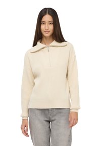 Kremowy sweter z prążkowanej dzianiny z pół zamkiem i szerokim kołnierzem, w połączeniu z jasnoszarymi dżinsami. Miękka tekstura i luźny krój.